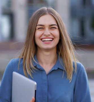 A smiling woman holding a laptop, exuding confidence and positivity in a professional setting.