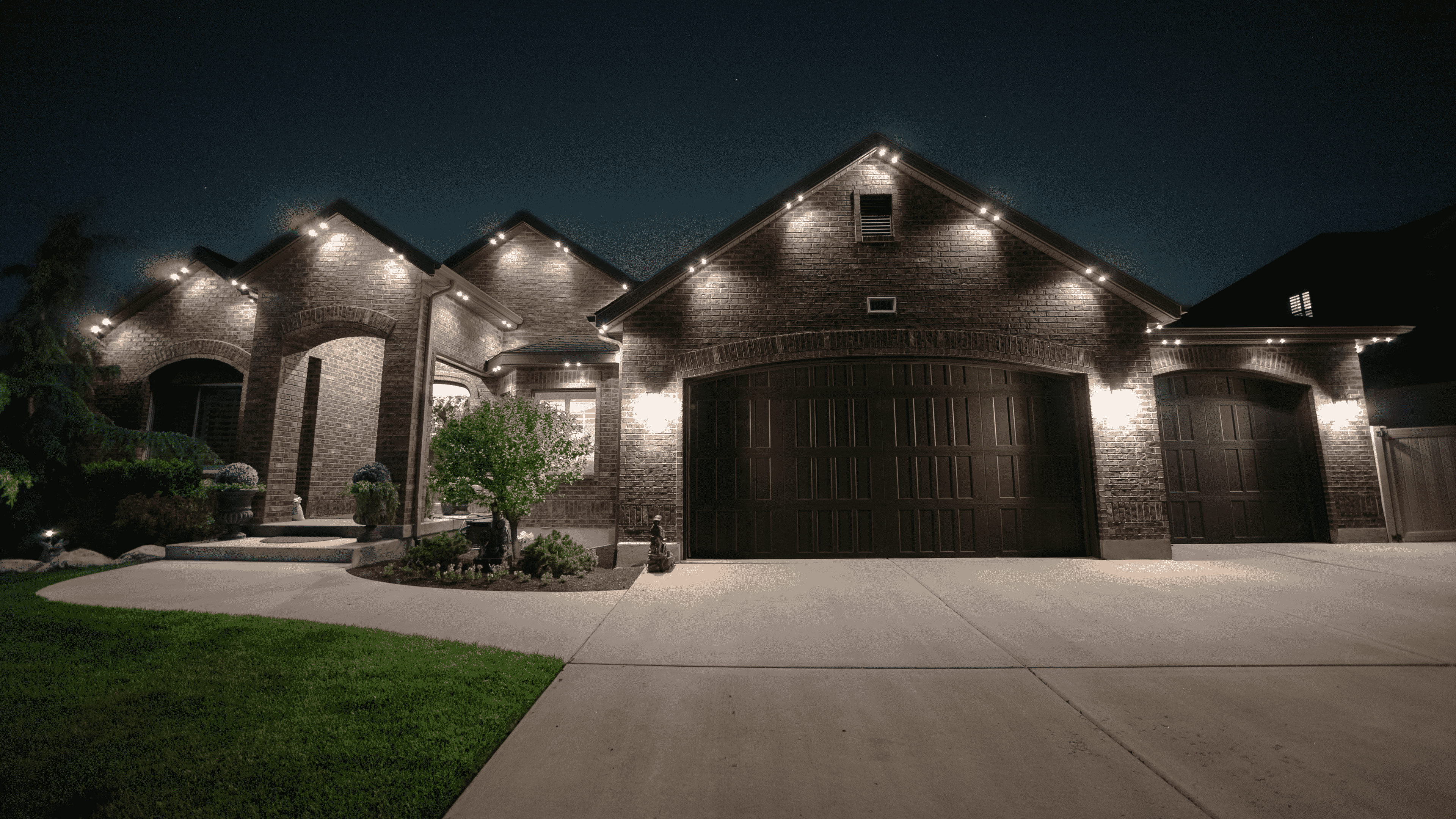 A charming residence featuring bright lights adorning the garage and driveway, enhancing its inviting appearance at night.