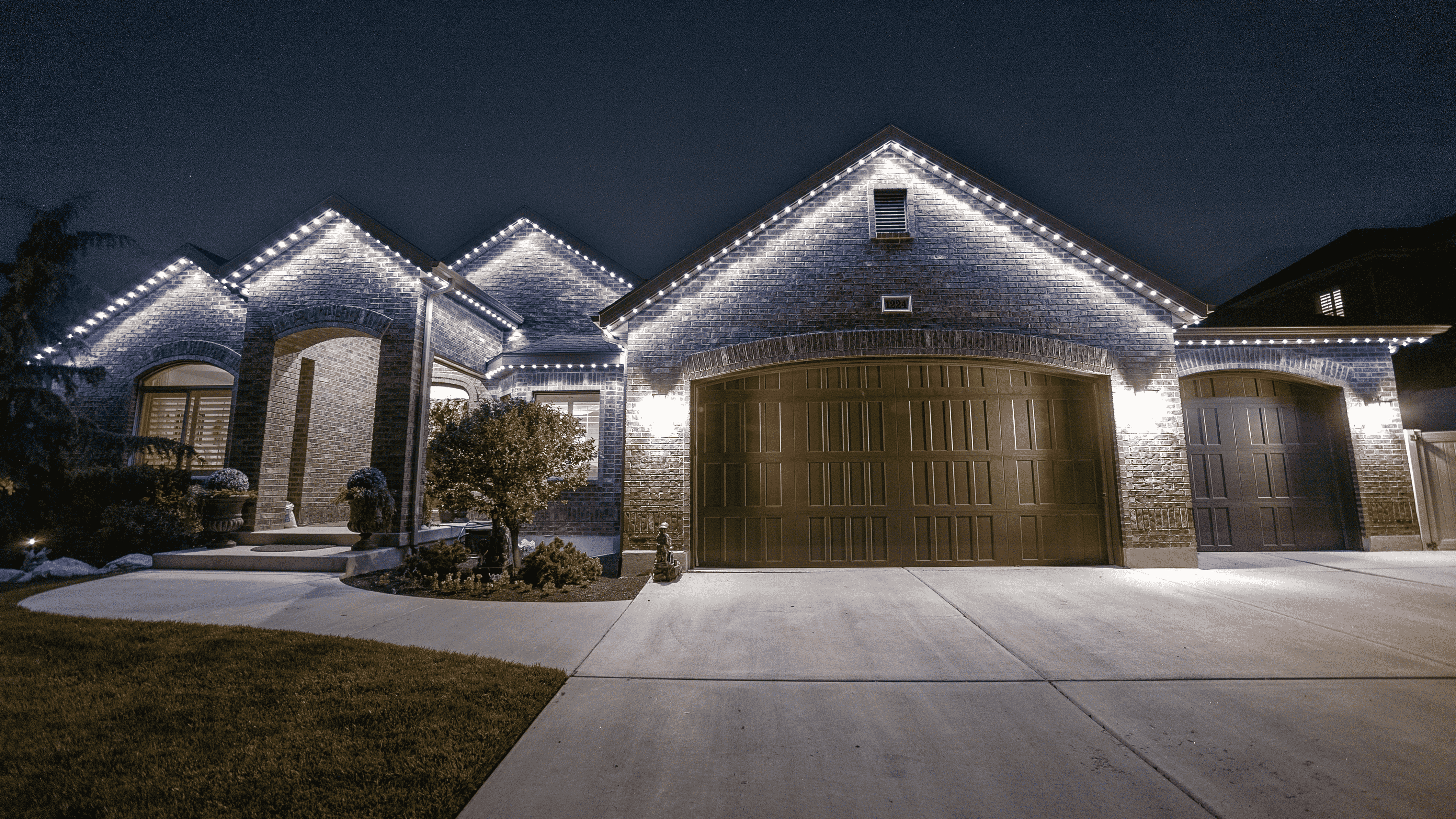 A charming residence featuring white lights on the garage and driveway, enhancing the home's welcoming appearance at night.