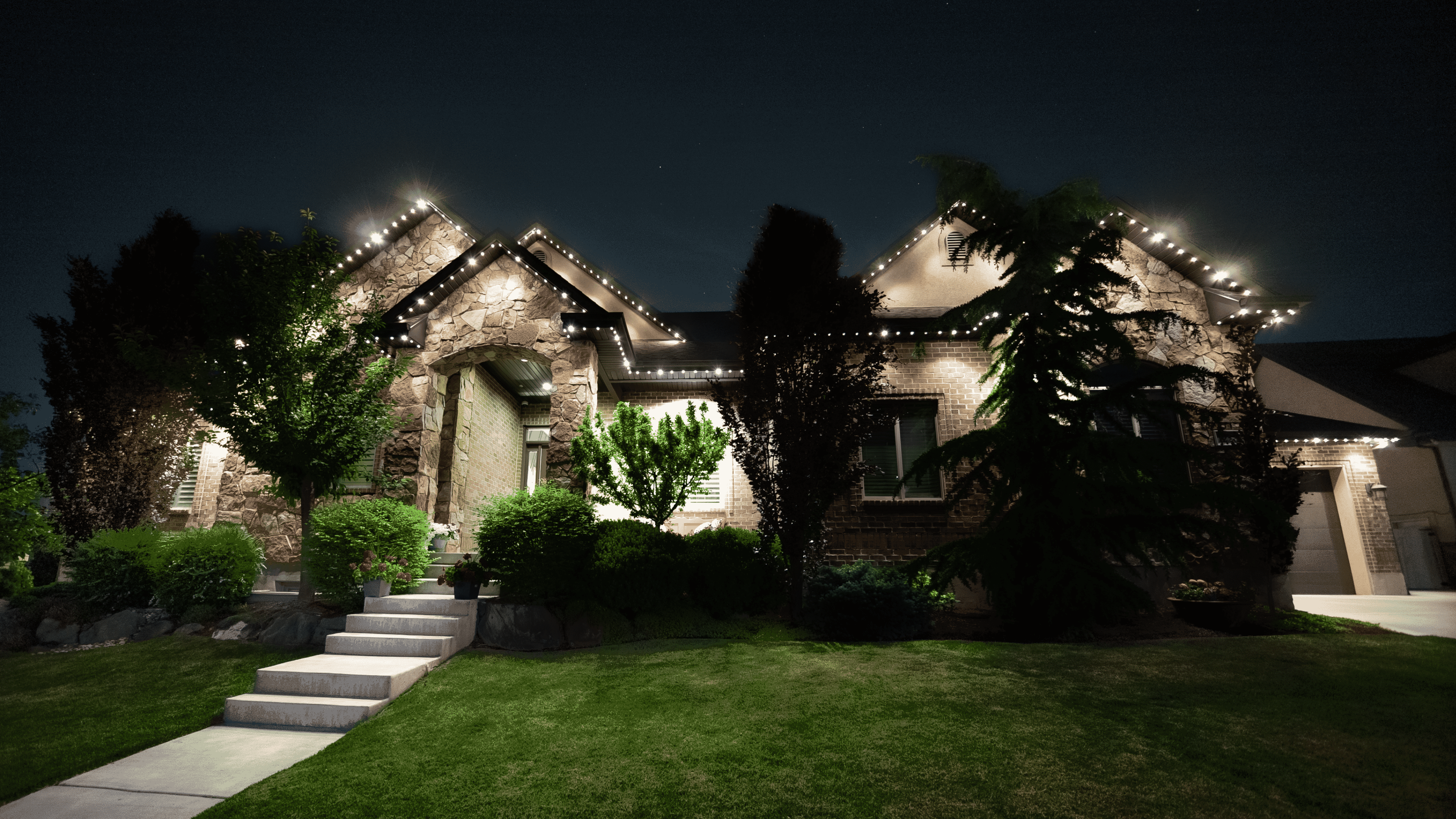 A charming house illuminated by lights adorning the front lawn, creating a warm and inviting atmosphere.